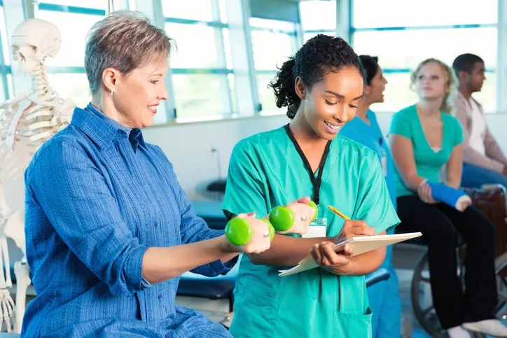 Physical therapist writing in chart during senior patient's physical therapy session