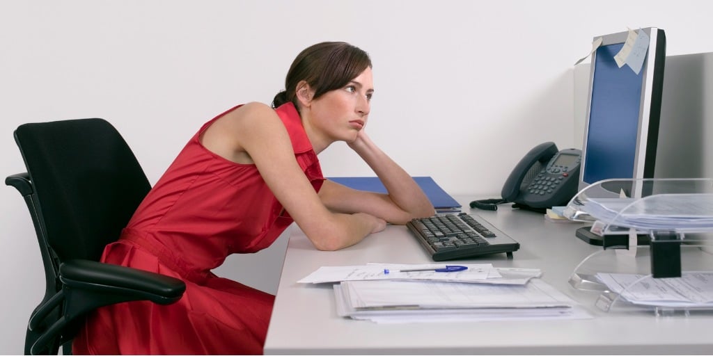 Side view of a female office worker slouching with bad posture and looking at notes on computer monitor at desk, cause of neck pain concept