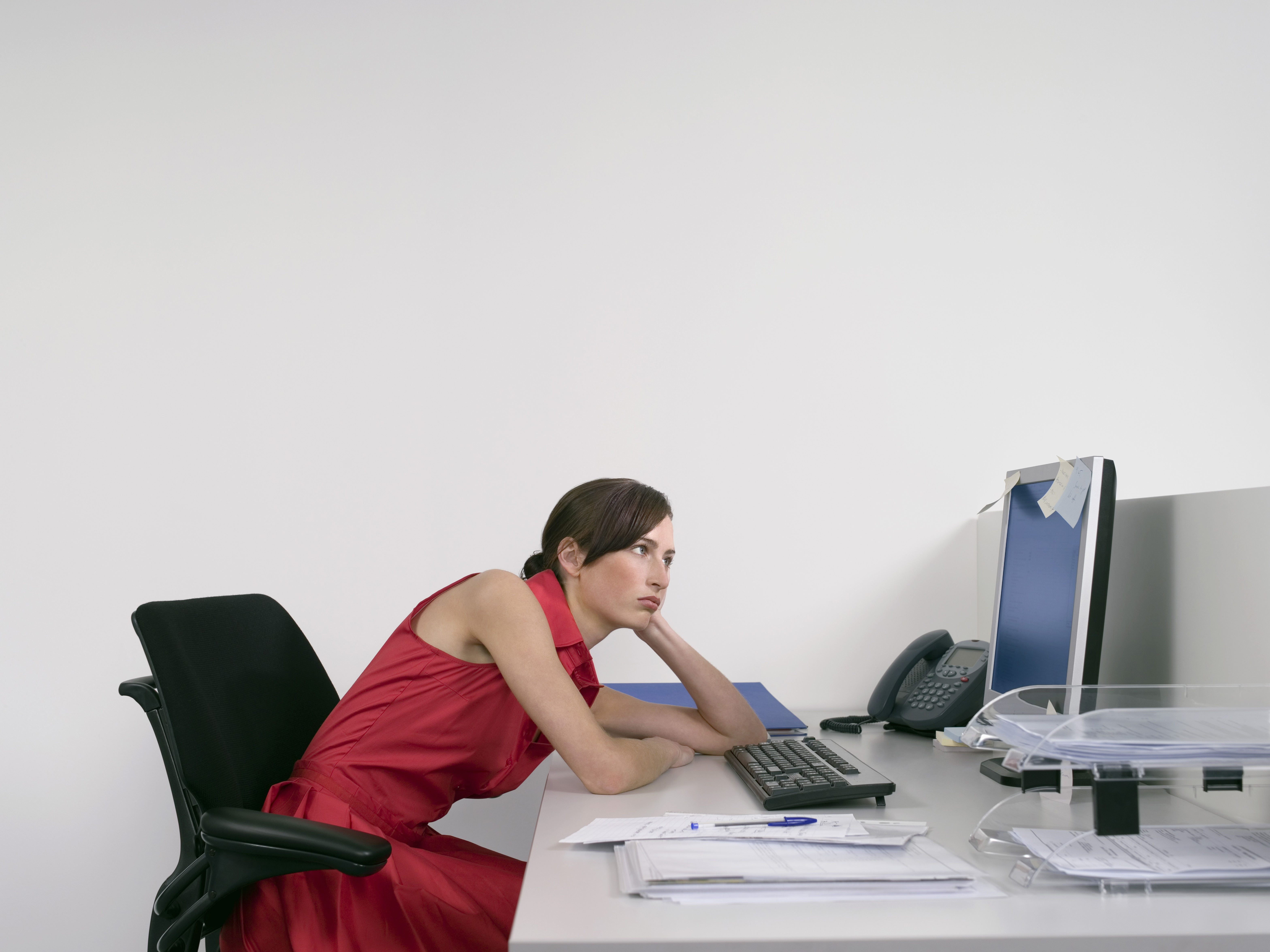 Side view of a female office worker slouching with bad posture and looking at notes on computer monitor at desk, cause of neck pain concept