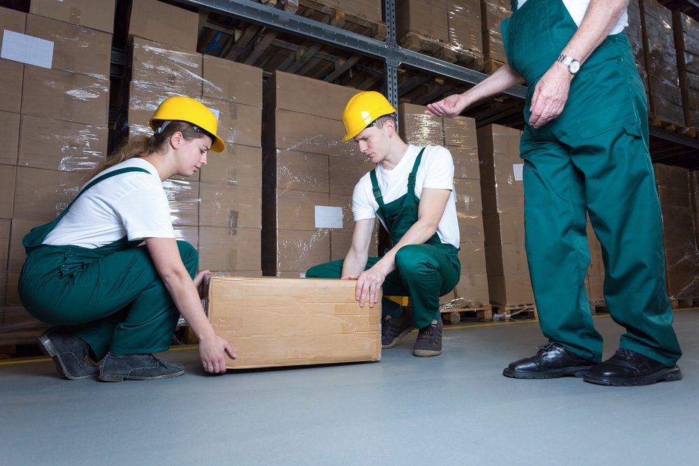 Two young workers lifting heavy box in warehouse. this can cause Work-Related Musculoskeletal Disorders