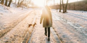 woman walking down a winter road with a small dog.health benefits from walking concept