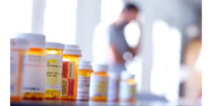 Line of prescription medications and opioids with man in the background wishing he could heal naturally