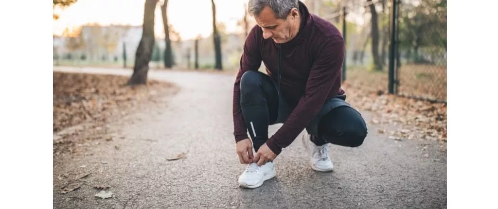 Senior man with the right footwear for foot pain, taking a pause from jogging to tie his shoelace