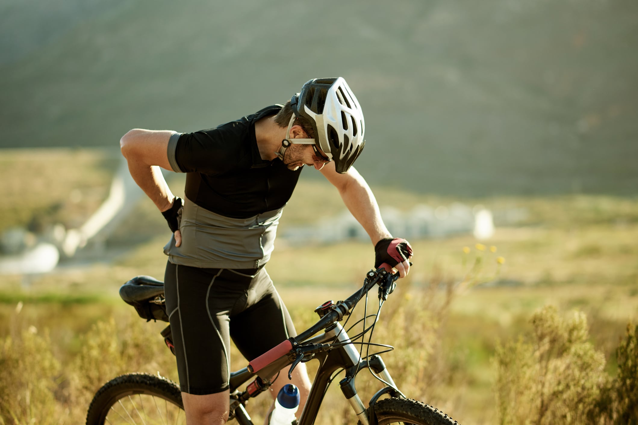 Shot of a mature man experiencing back pain while out for a ride on his mountain bike