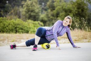 young woman foam rolling her hips before exercising outdoors
