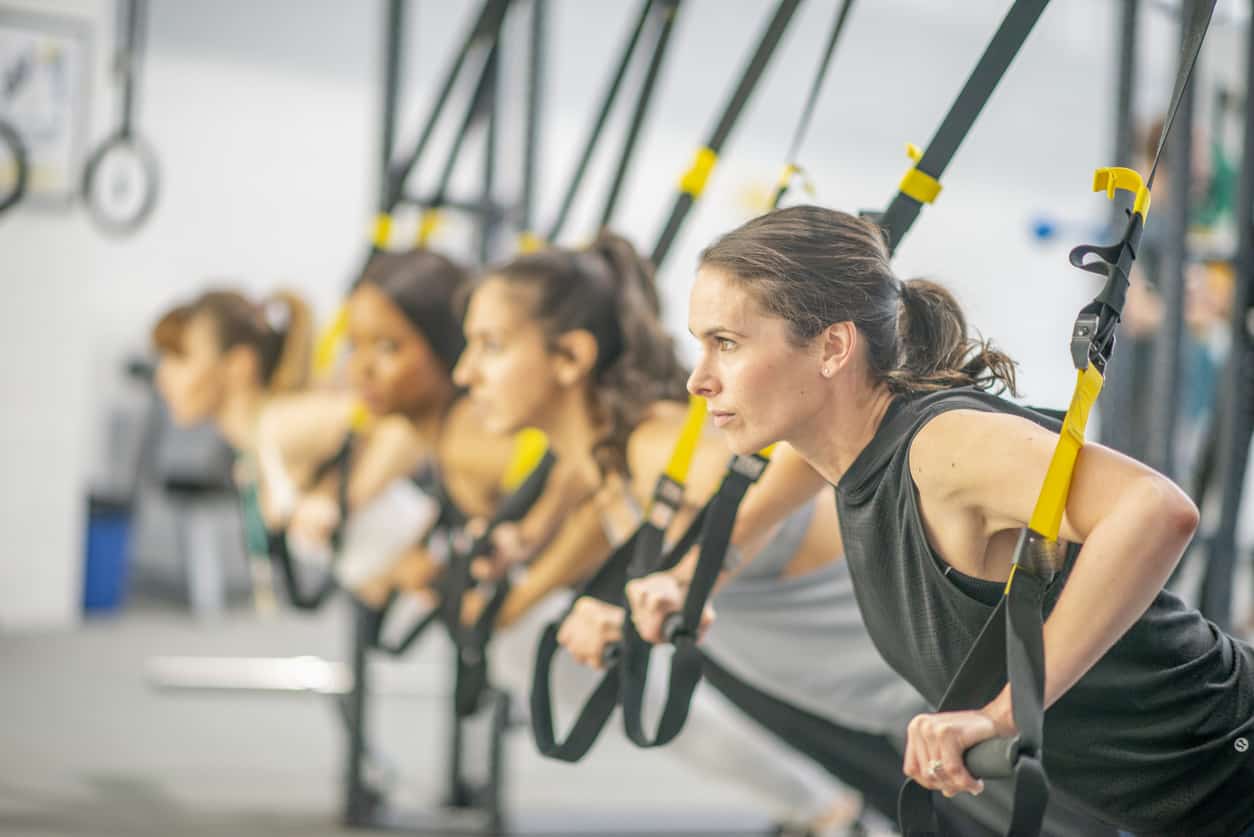 Group of women in a gym using suspended resistance bands in their core strengthening exercises.