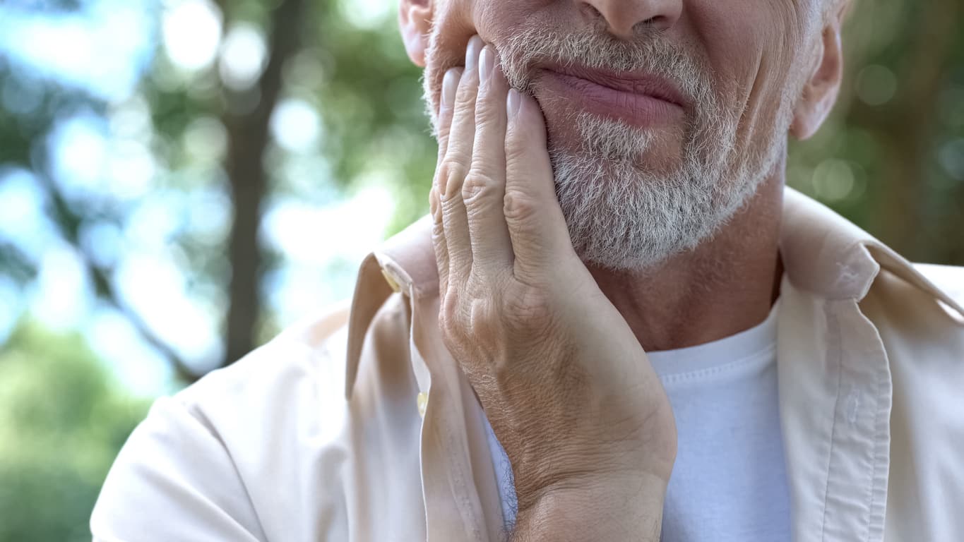 Senior man touching his jaw - showing pain experienced from TMJ disorders.
