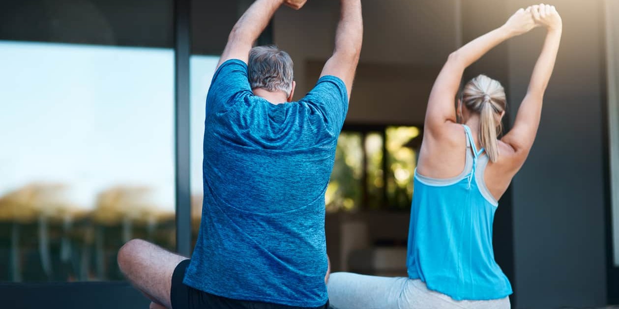 Mature couple at home doing stretching exercises to combat and relieve lower back pain.