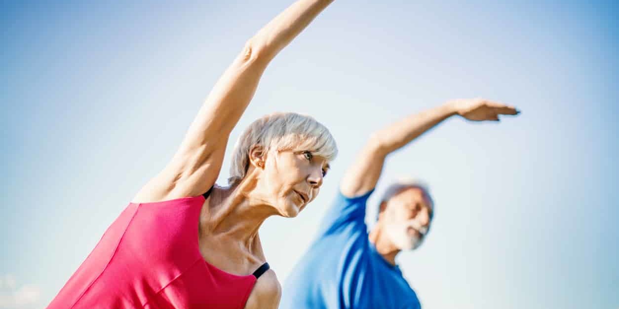 Mature couple doing stretching exercises outside - relieving shoulder pain.