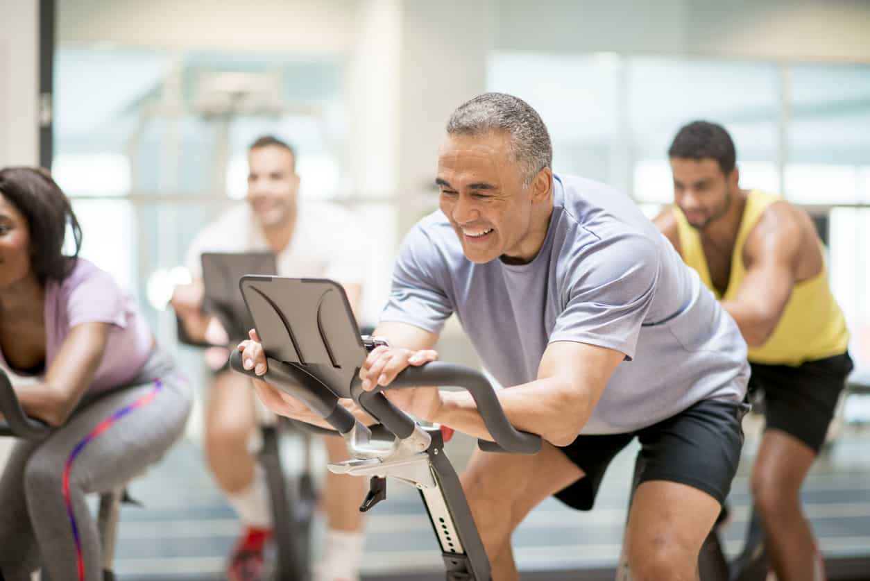 Adult man enjoying a cycling class in a fitness gym after undergoing Class IV Laser Therapy treatment for his injuries.