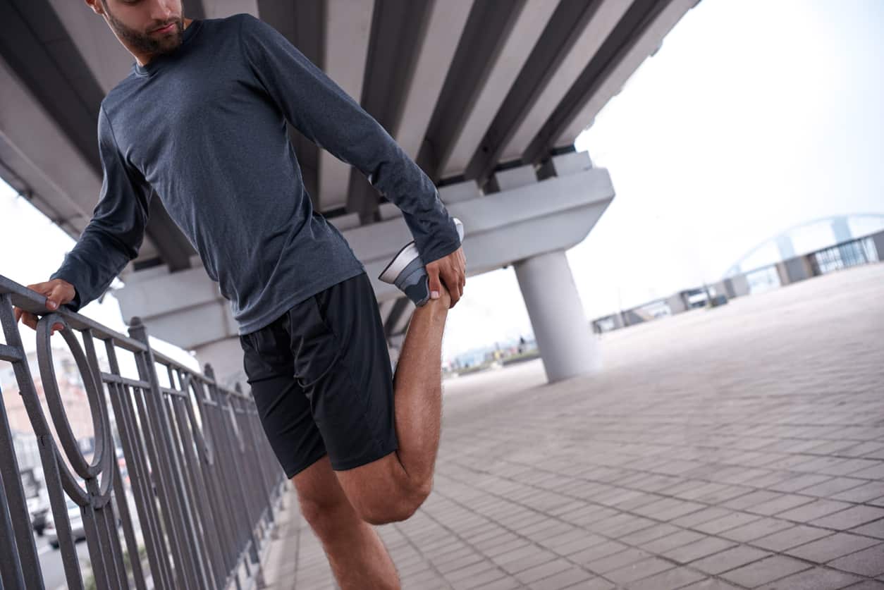 Male runner stretching his ankle prior to running - improving ankle mobility.