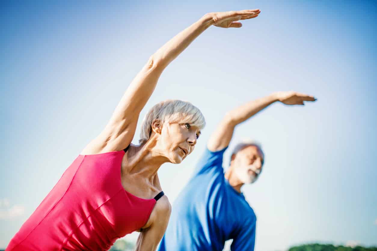 Mature couple doing stretching exercises outside - relieving shoulder pain.