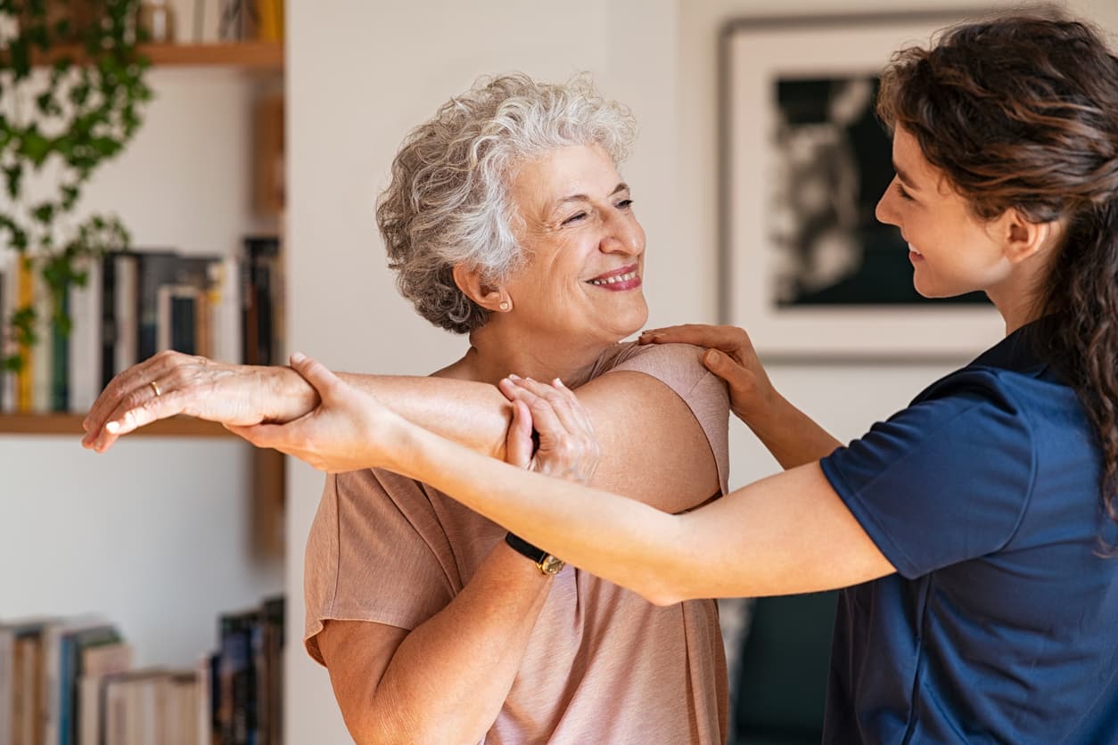 Female therapist assisting a mature woman in exercising - providing physical therapy for pain and injuries.