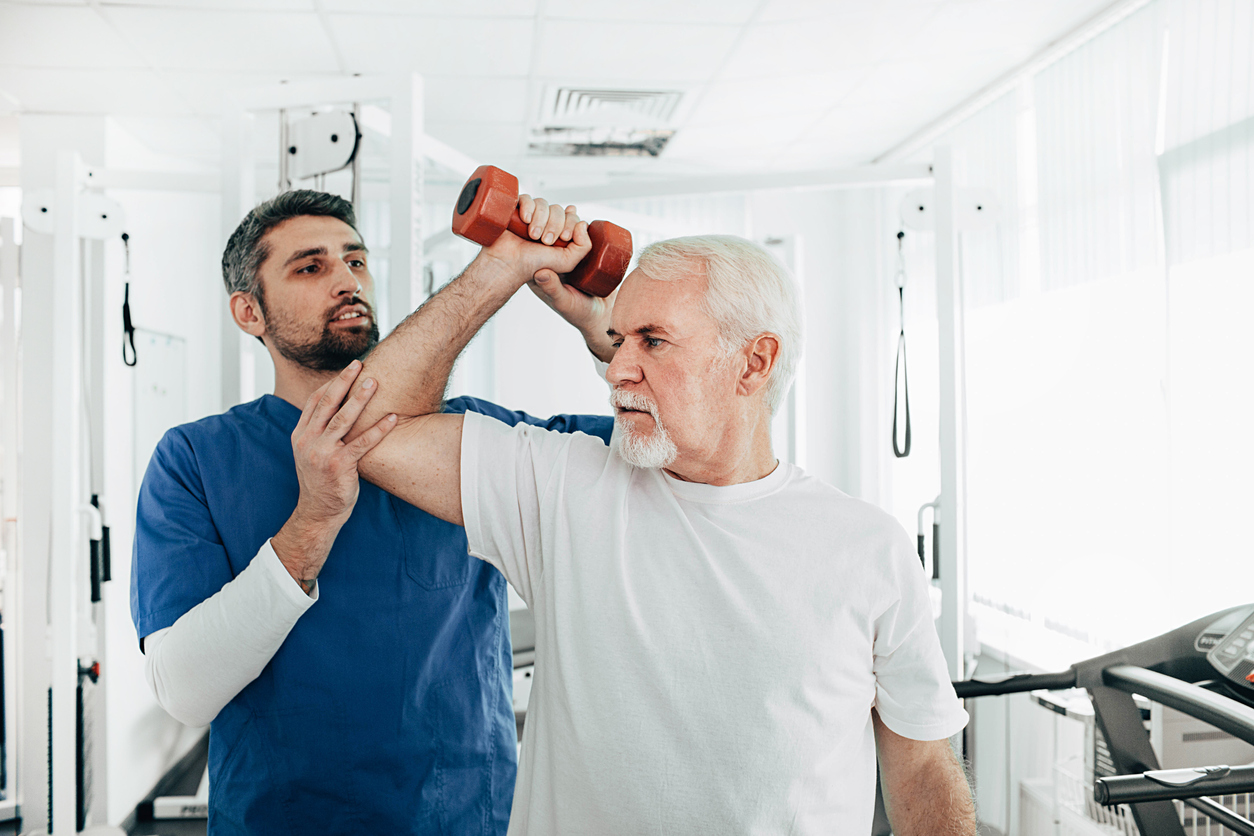 Male therapist assisting a senior man during a physical therapy program.