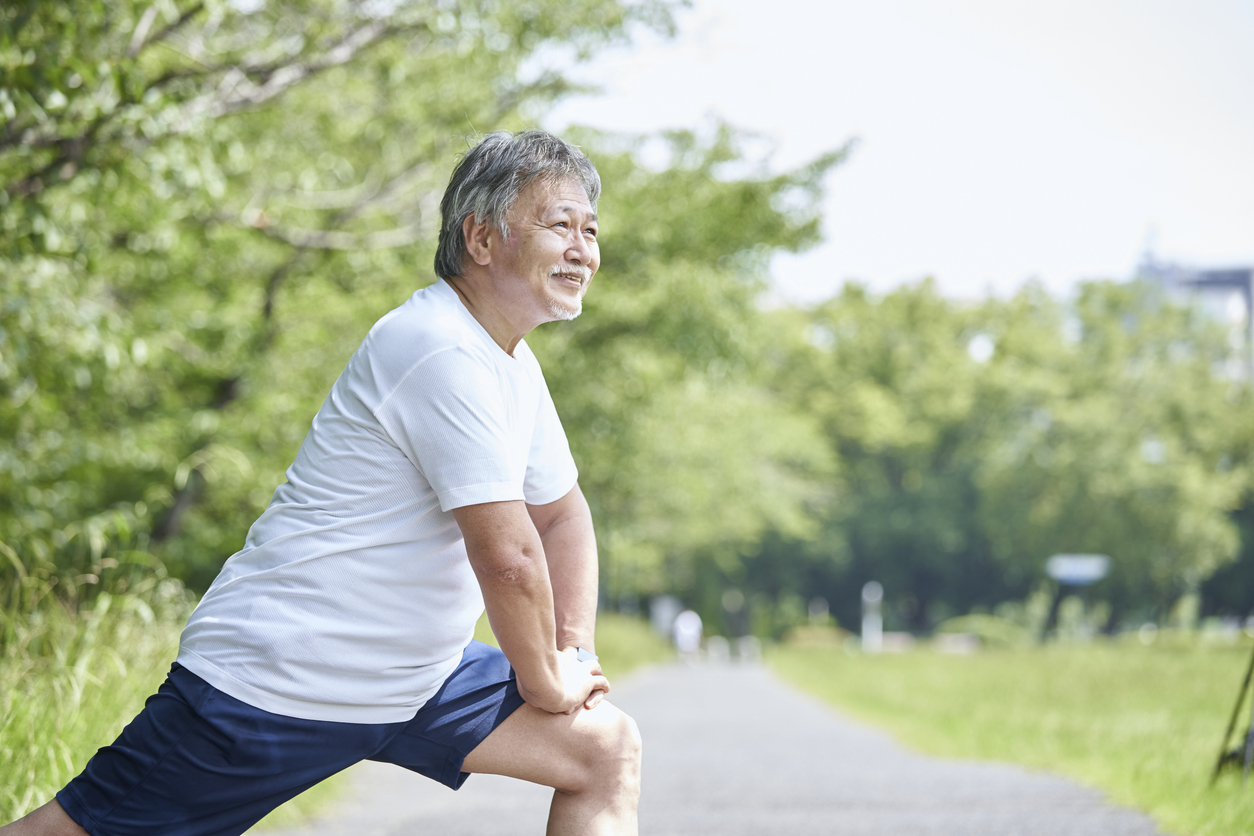 Senior man stretching outdoors - relieving symptoms of low back pain.