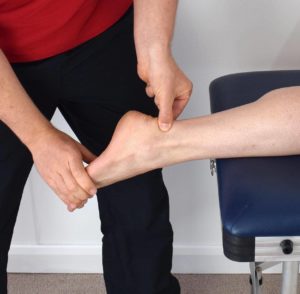 A physical therapist physically manipulating a patient’s Achilles tendon