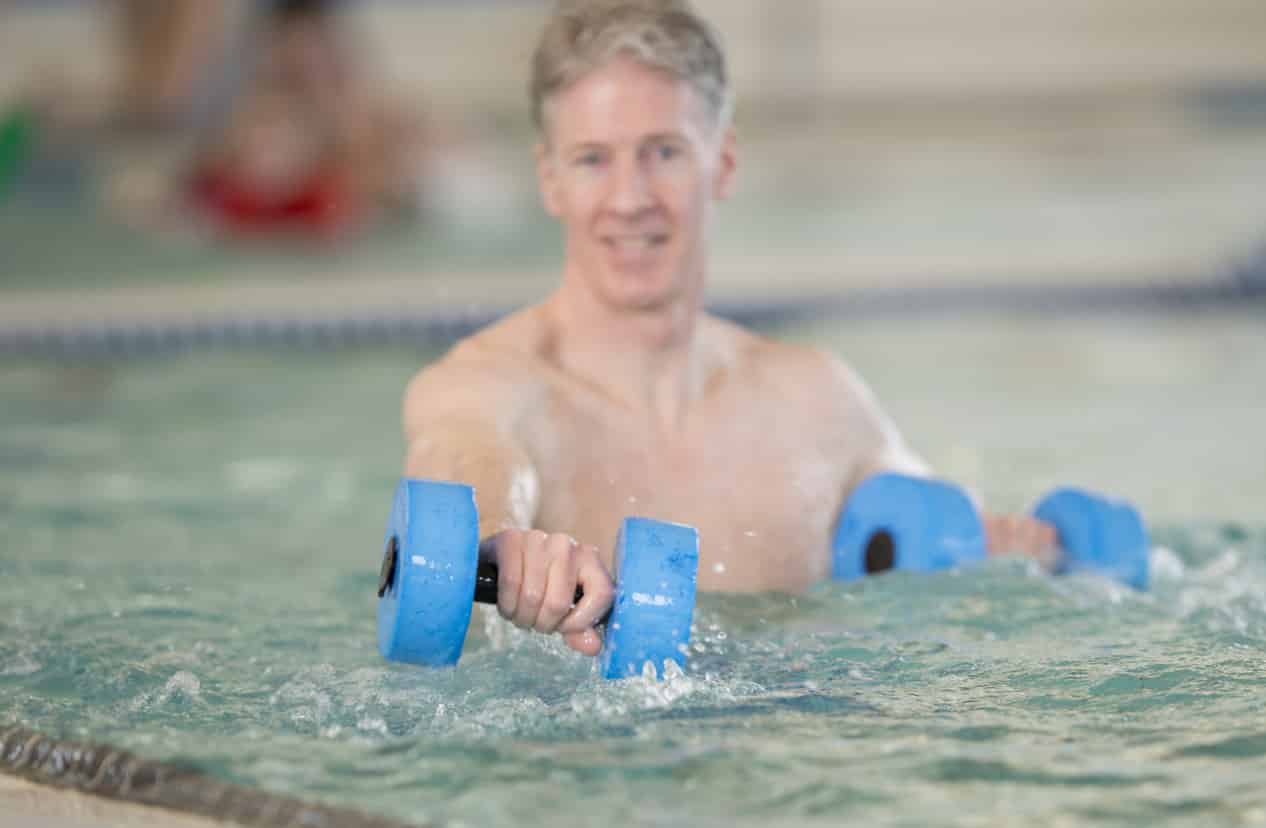 Adult man using water dumbbells while performing aquatic therapy exercises in the pool
